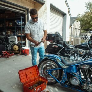 A man working on a motorcycle in a garage, surrounded by tools and engine parts.